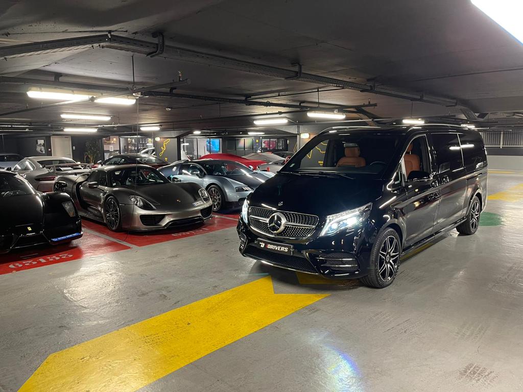 Une camionnette Mercedes noire est garée dans un garage, entourée de voitures de sport.
