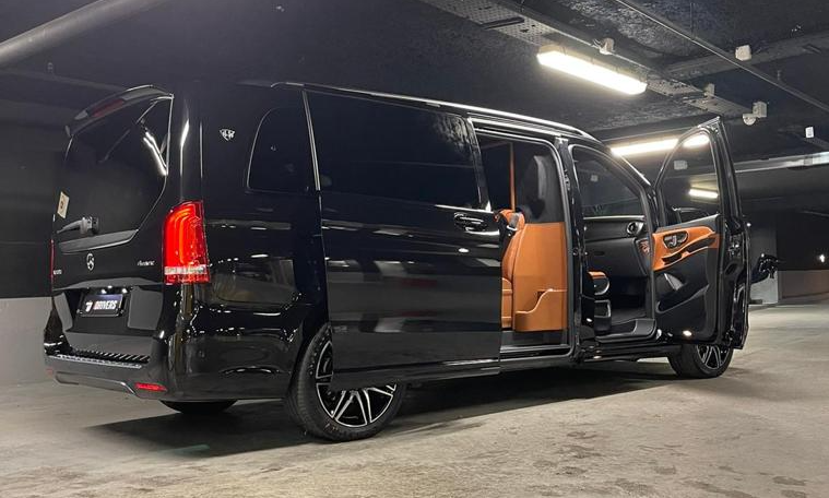 Fourgonnette noire aux portes ouvertes, laissant apparaître un intérieur marron, garée dans un parking souterrain.