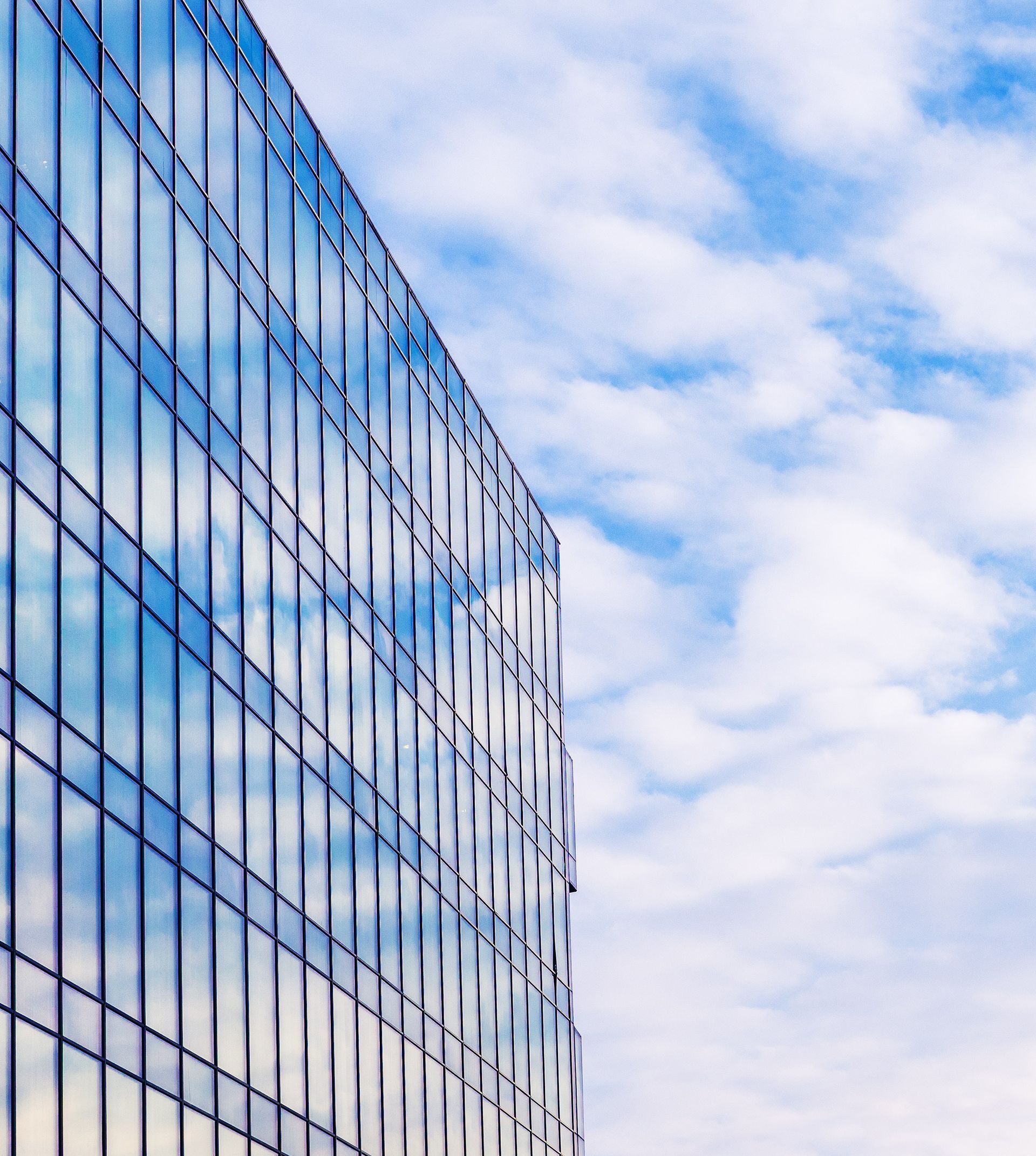 A tall building with a lot of windows against a blue sky with clouds