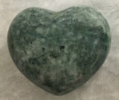 A Green Heart-Shaped Stone Resting on A White Cloth — Crystal Cauldron In South Mackay, QLD