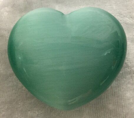 A Green Heart-Shaped Stone Resting on A White Cloth — Crystal Cauldron In South Mackay, QLD