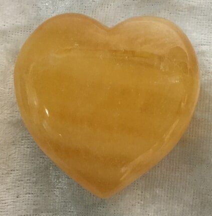 A Yellow Heart-Shaped Stone Resting on A White Cloth — Crystal Cauldron In South Mackay, QLD