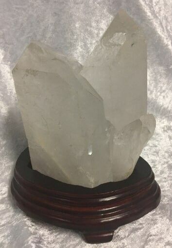 A Large, Clear Quartz Crystal Cluster Rests on A Dark Wooden Base — Crystal Cauldron In South Mackay, QLD