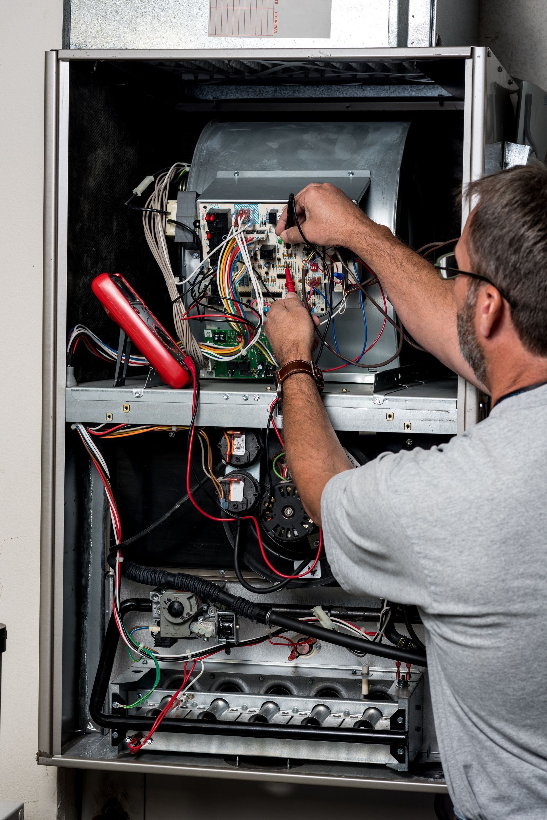 Mechanic works on a home furnace with volt meter 