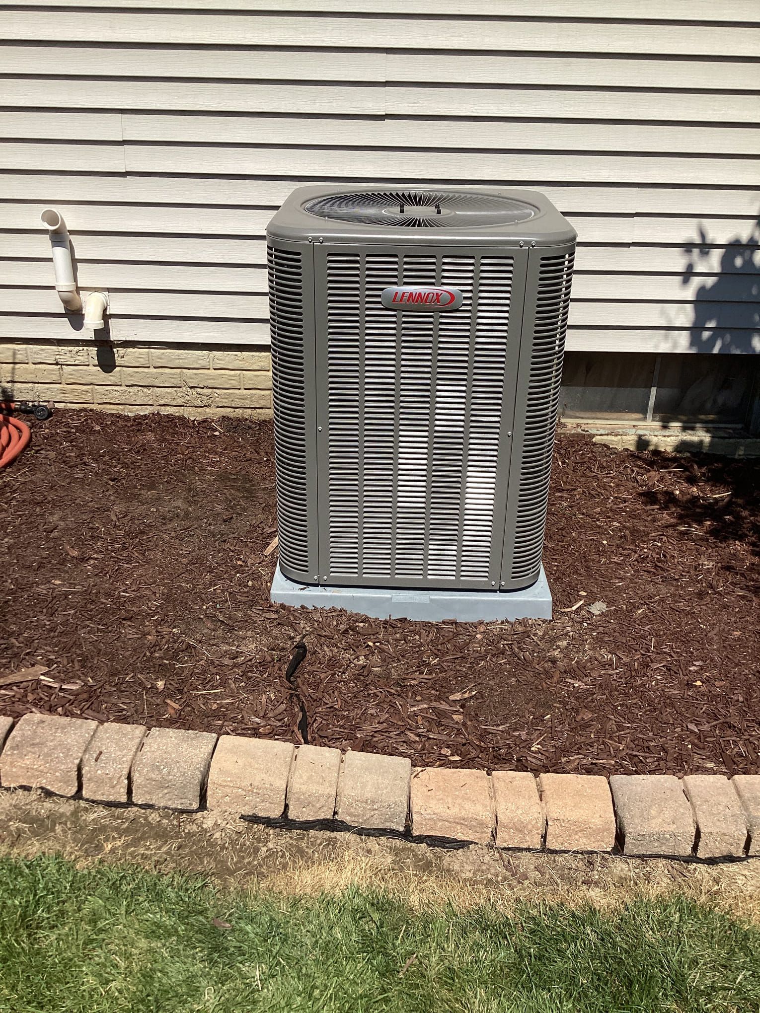An air conditioner is sitting on top of a pile of mulch in front of a house.
