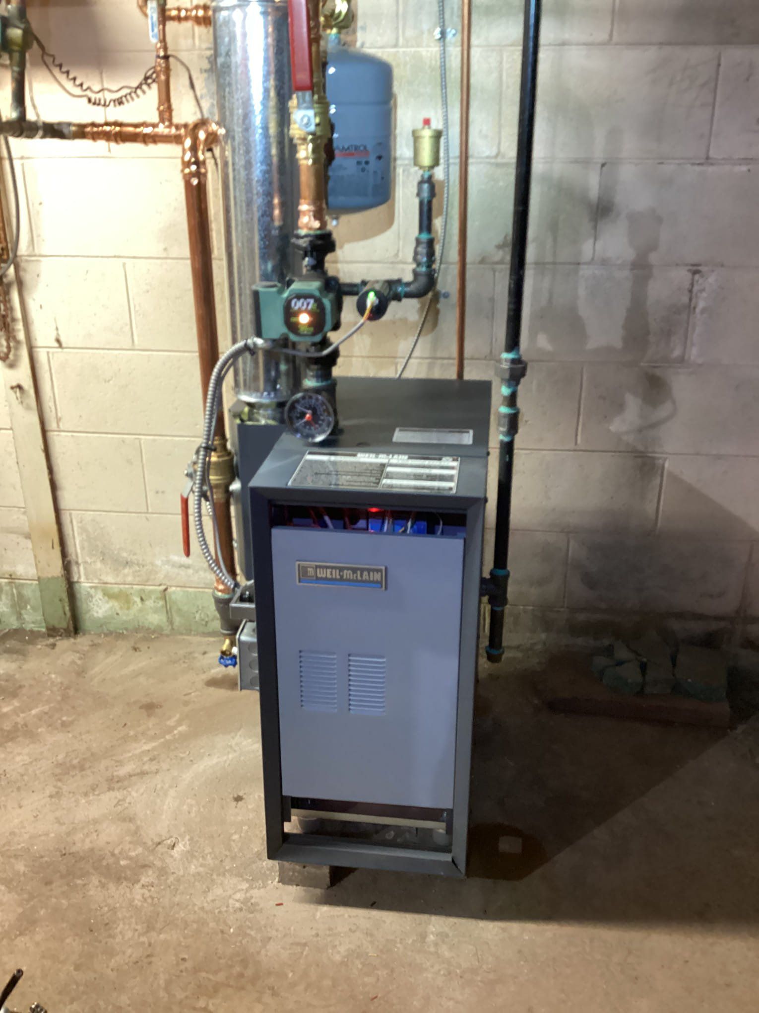 A boiler is sitting in a basement next to a brick wall.