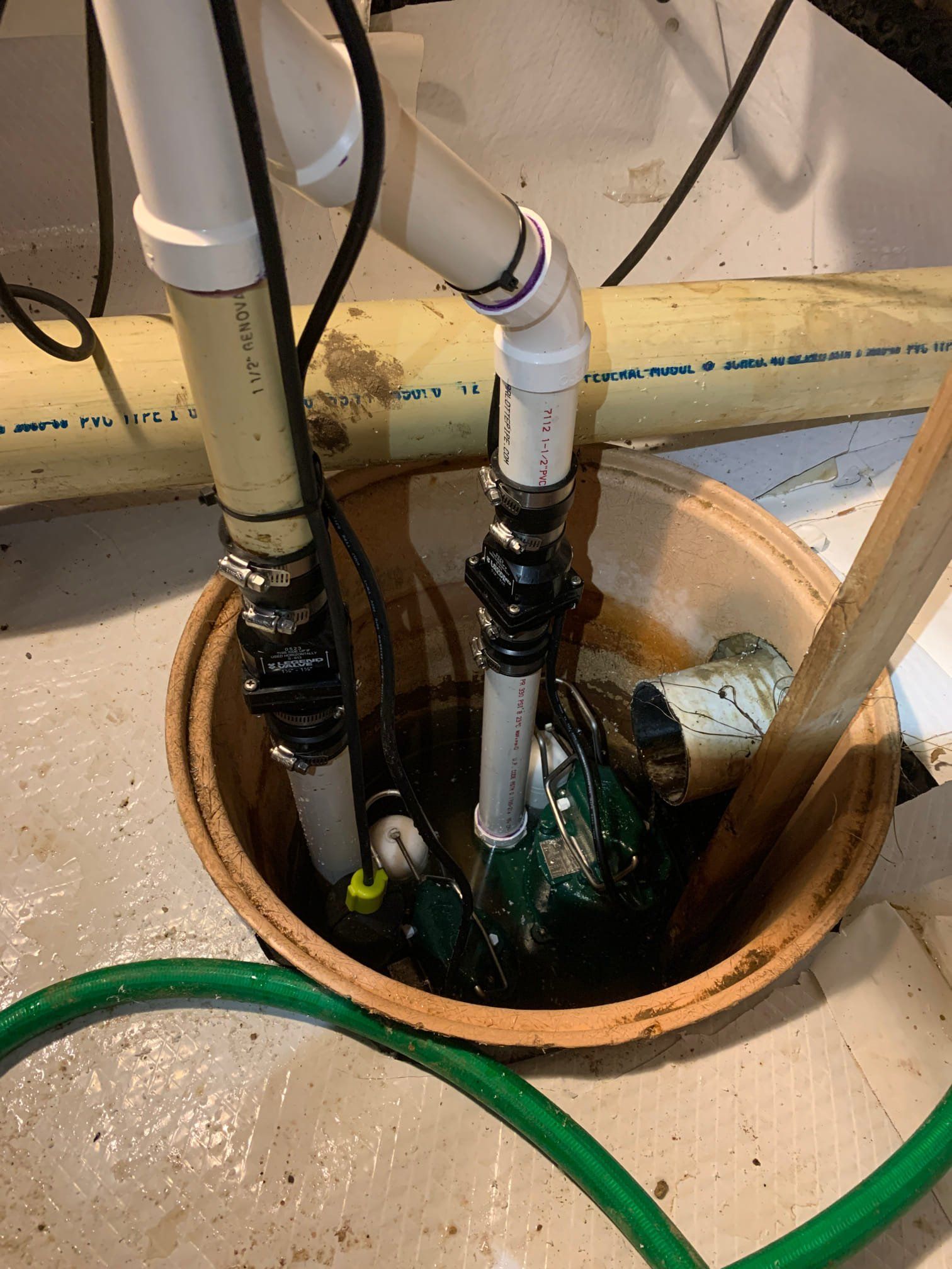 A green hose is connected to a sump pump in a basement.