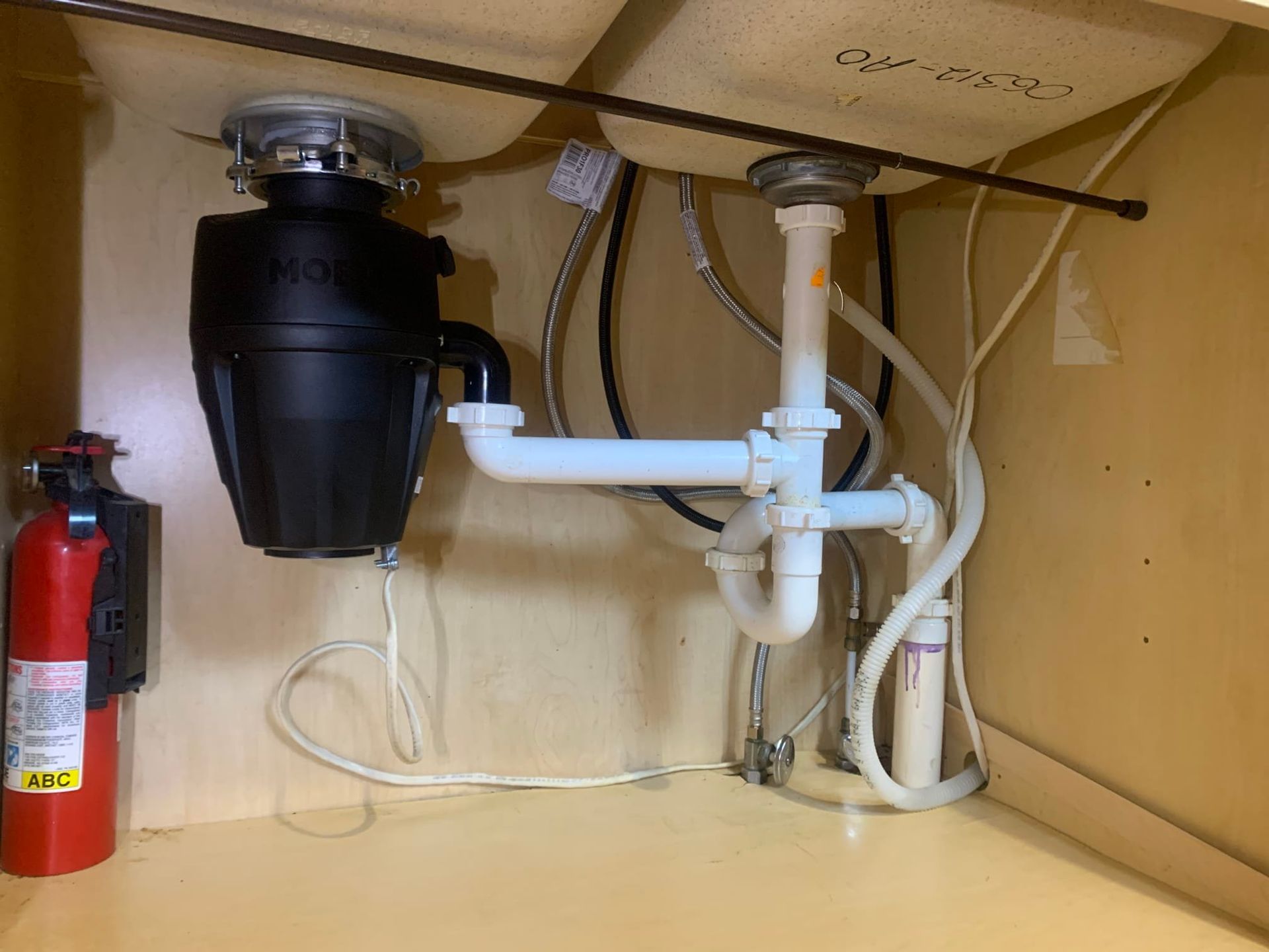 A sink with a garbage disposal and a fire extinguisher underneath it.