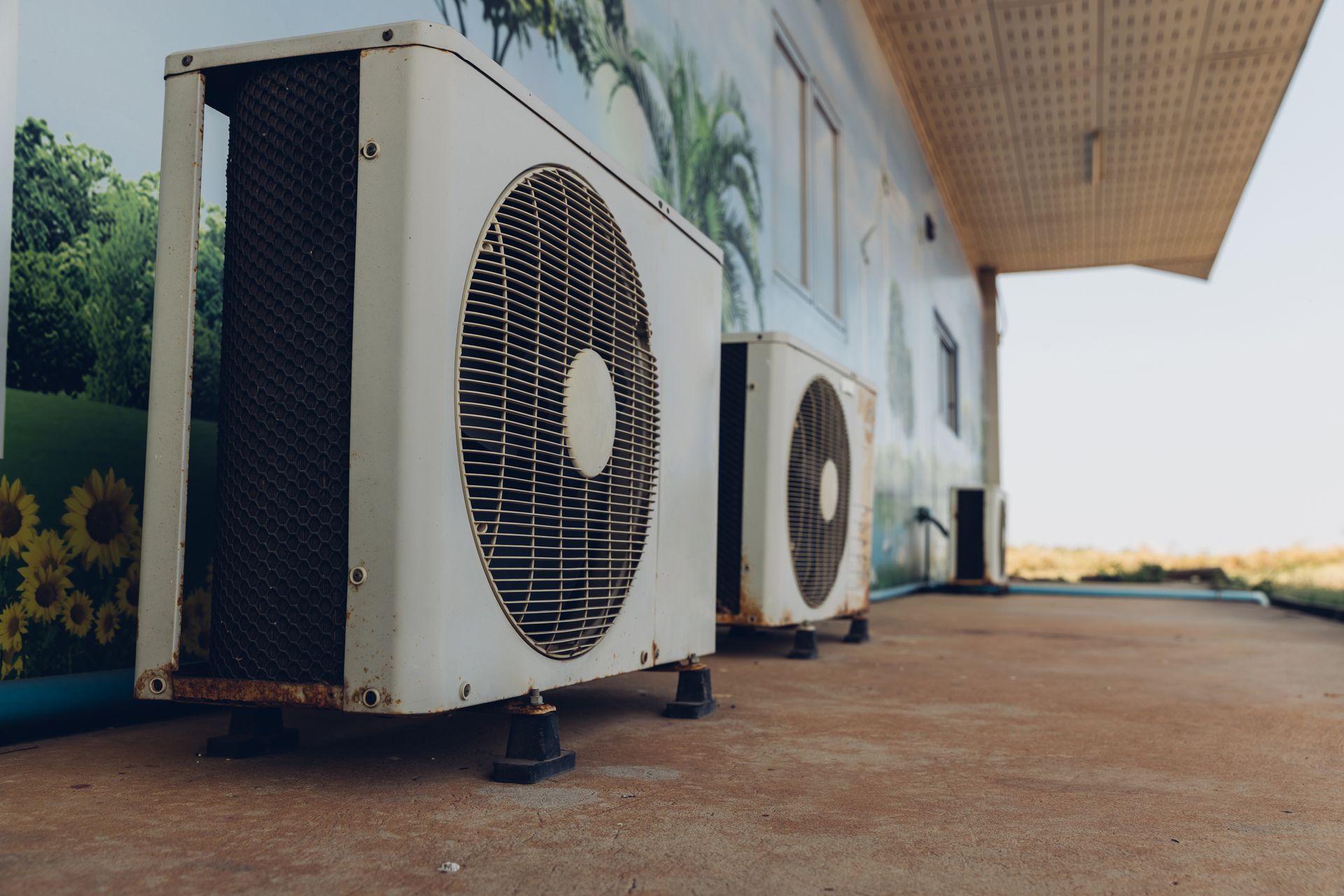 Outdoor HVAC units beside building with sunflower mural, showcasing energy-efficient cooling.