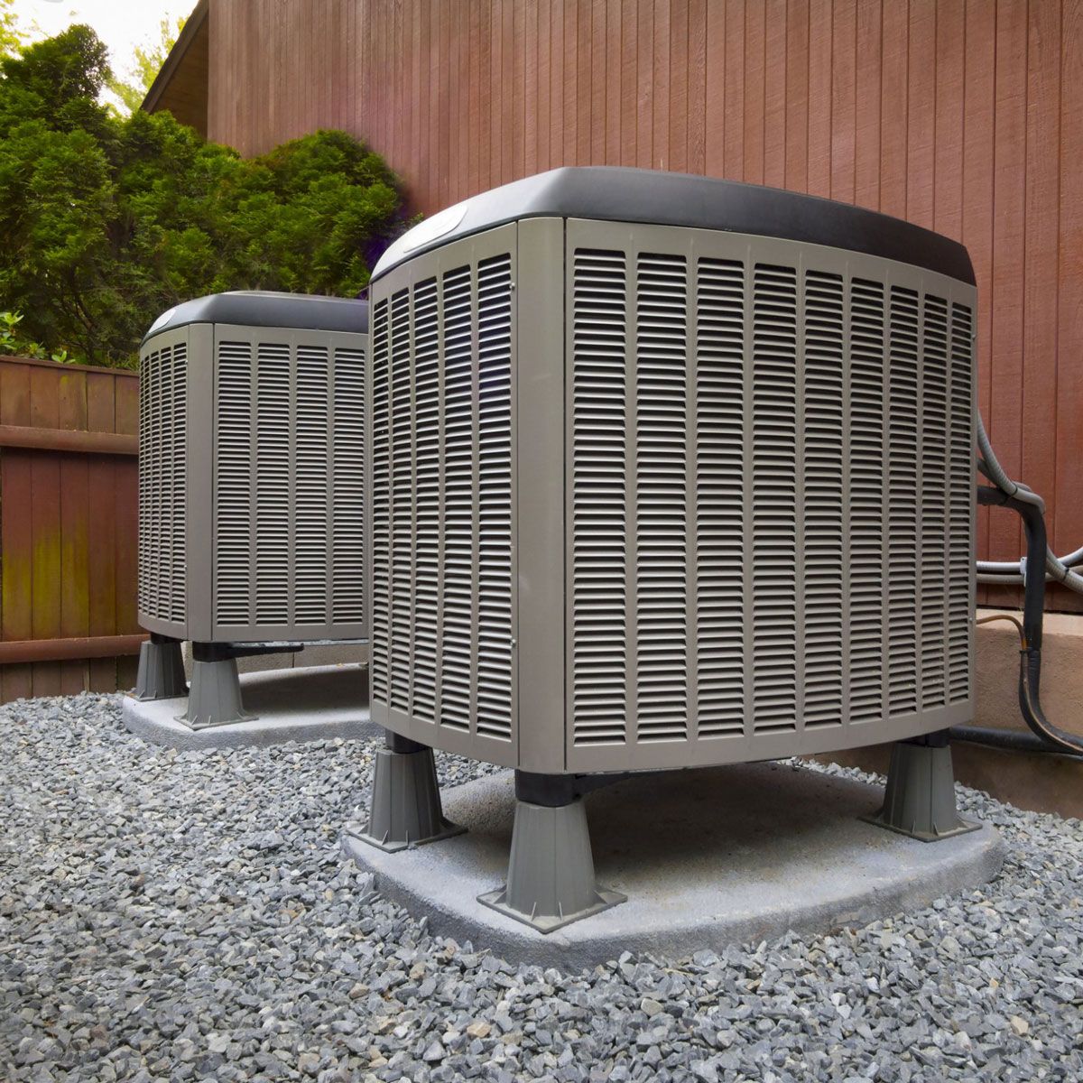 Two air conditioners are sitting on gravel outside of a house.