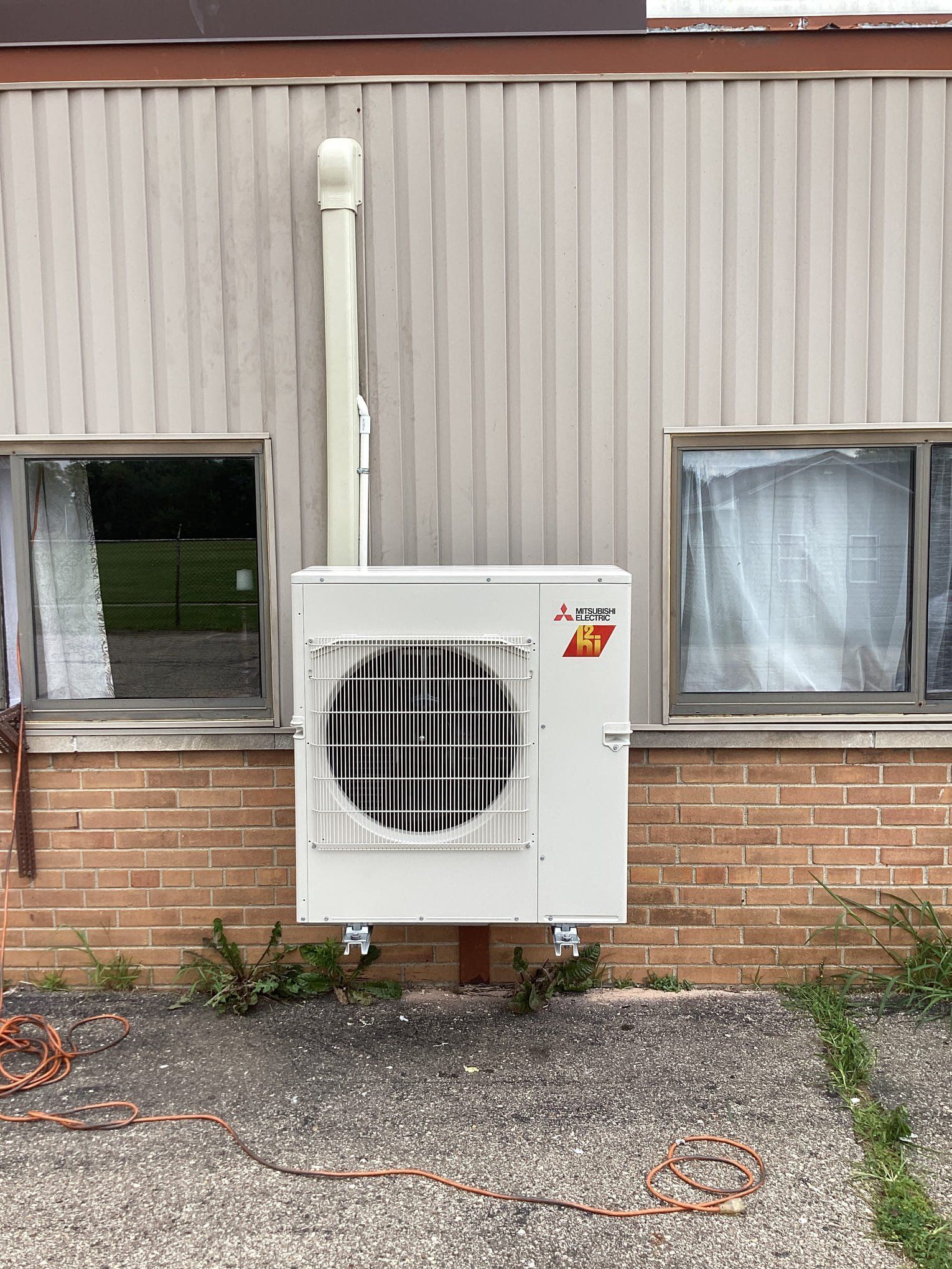 A white air conditioner is mounted on the side of a brick building.