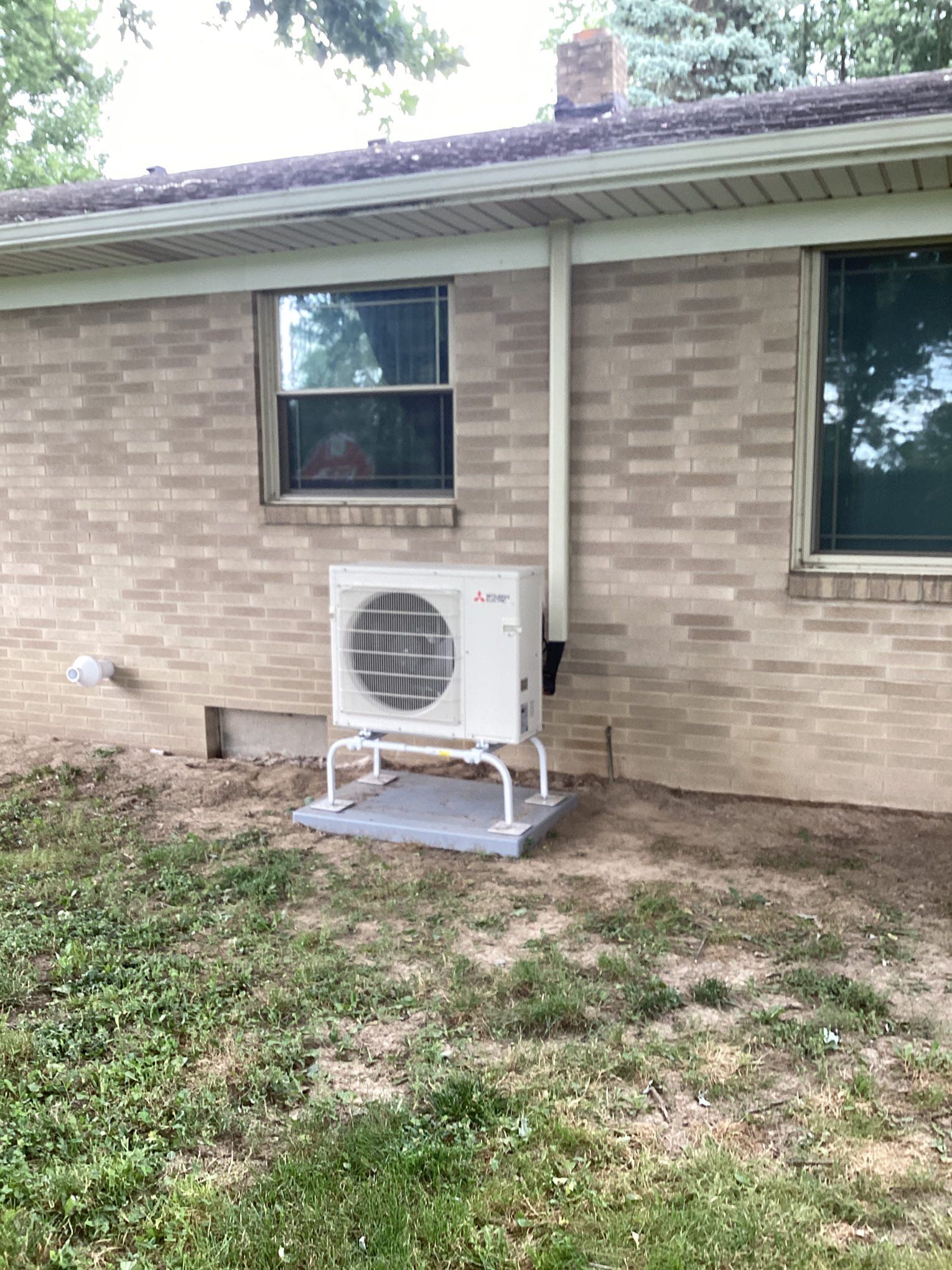 A white air conditioner is installed on the side of a brick house.