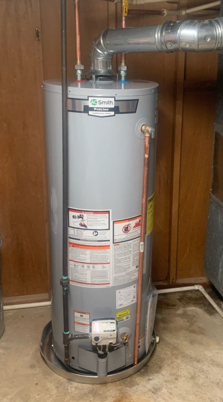 A water heater is sitting in a basement next to a wooden wall.