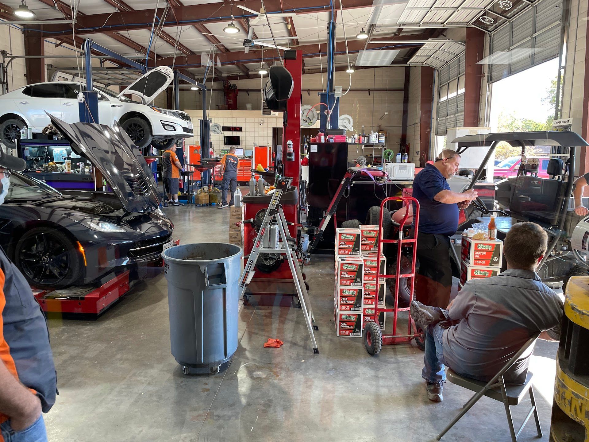Inside a car repair shop, cars on lifts, mechanics working, tools, parts, and a person giving instruction. | Vencam Auto Repair