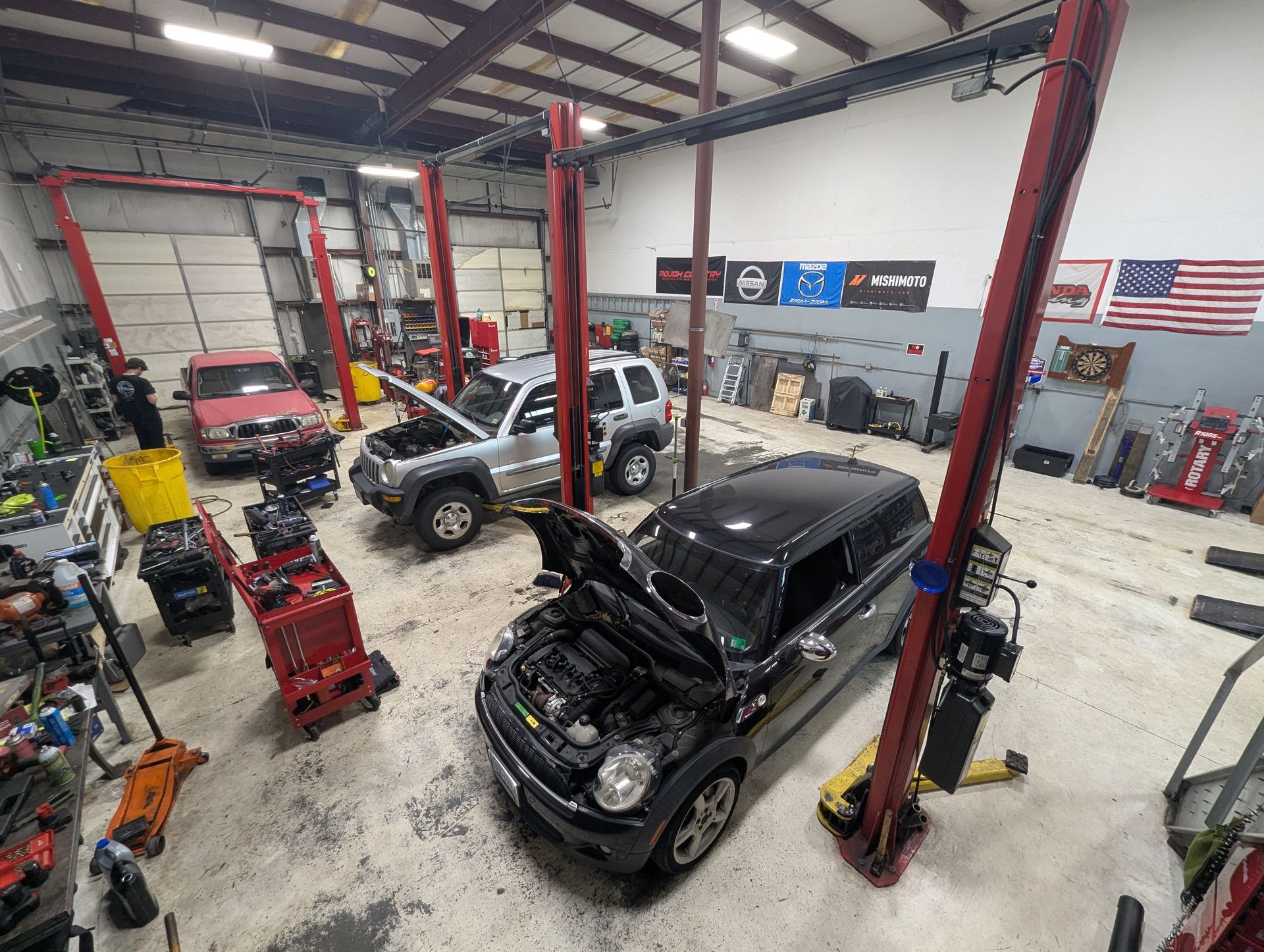 Cars in a mechanic shop with open hoods, lifted on red posts | Vencam Auto Repair