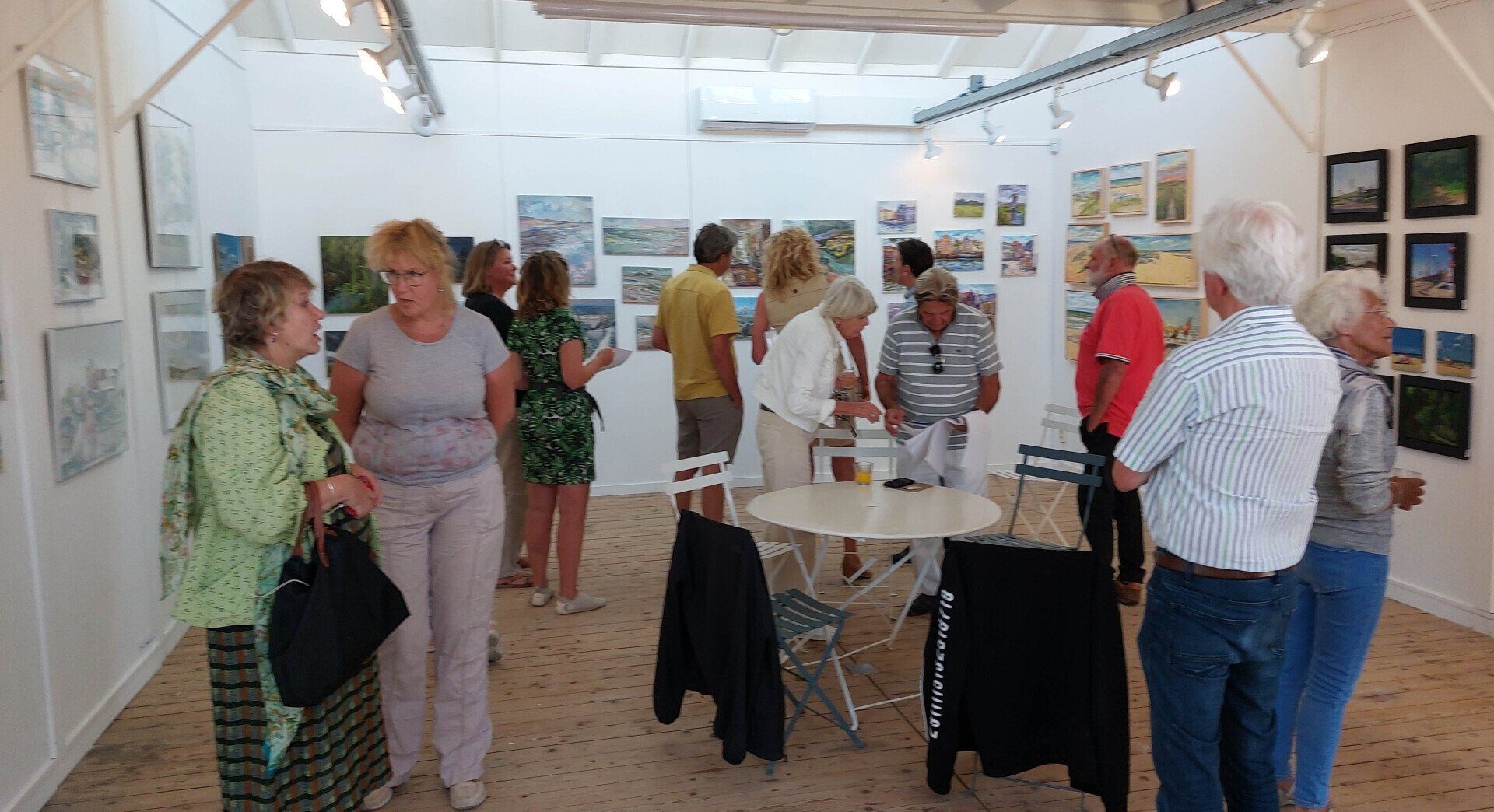 Een groep mensen bekijkt kunstwerken die aan de muren van een helder verlichte galerie hangen.