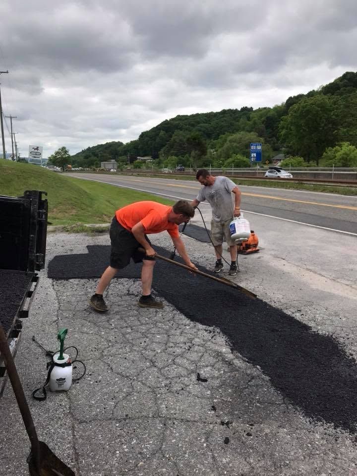 Two men are laying asphalt on the side of a road.