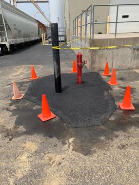 A fire hydrant is surrounded by orange cones in a parking lot.