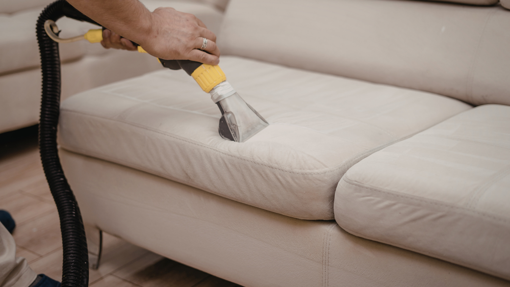 Hand using a vacuum upholstery tool to clean a beige sofa cushion