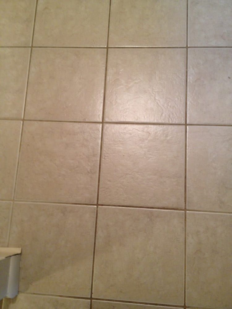 Beige tiled floor with grout lines and a small wall fixture at the lower left edge.