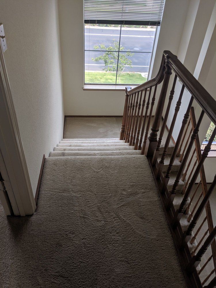 Carpeted stairway with wooden railing leading to a bright windowed landing