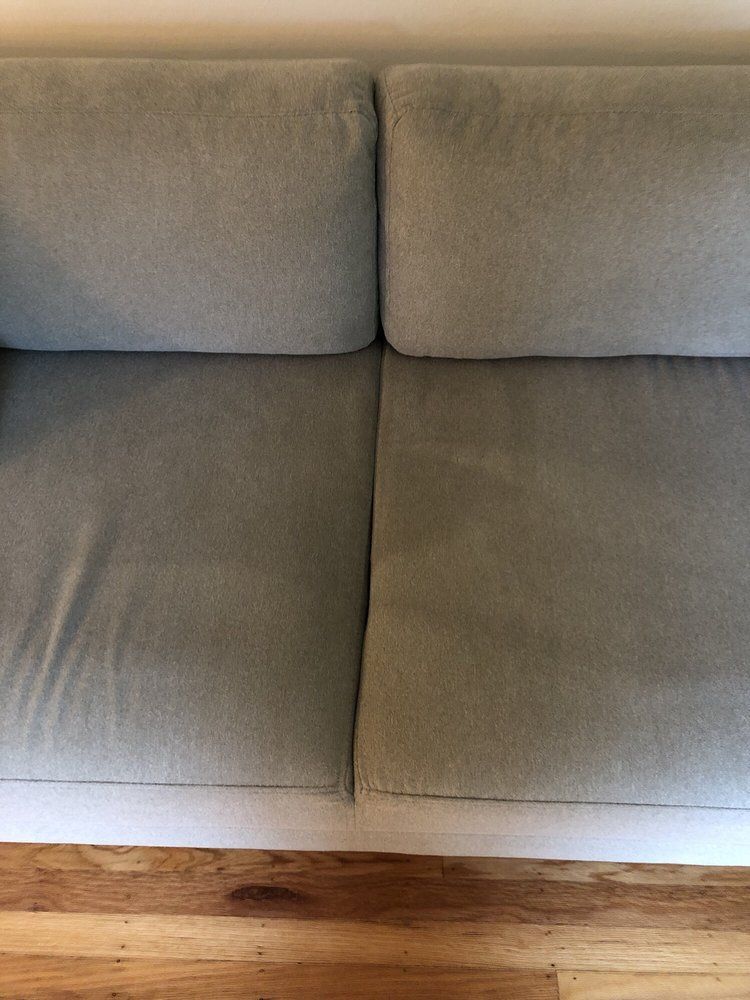 Gray upholstered sofa cushions above a wooden floorboard and baseboard