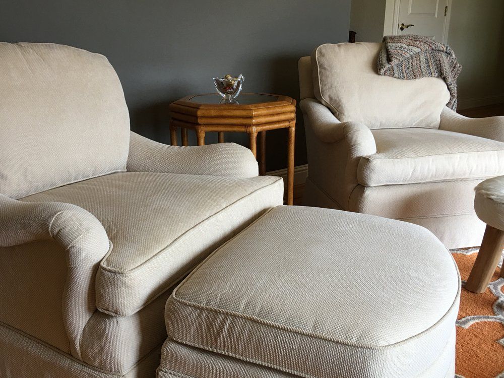 Cozy living room with cream armchairs, ottoman, and small wooden side table with a decorative bowl.