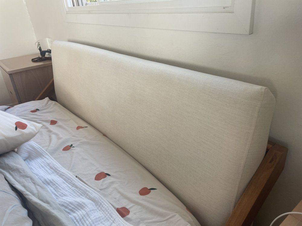 Small bedroom with a bed, white bedding, and a beige upholstered headboard under a window.