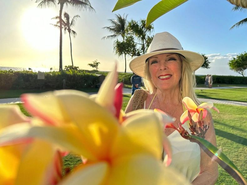 Woman in a straw hat holding flowers in a sunny garden at sunset