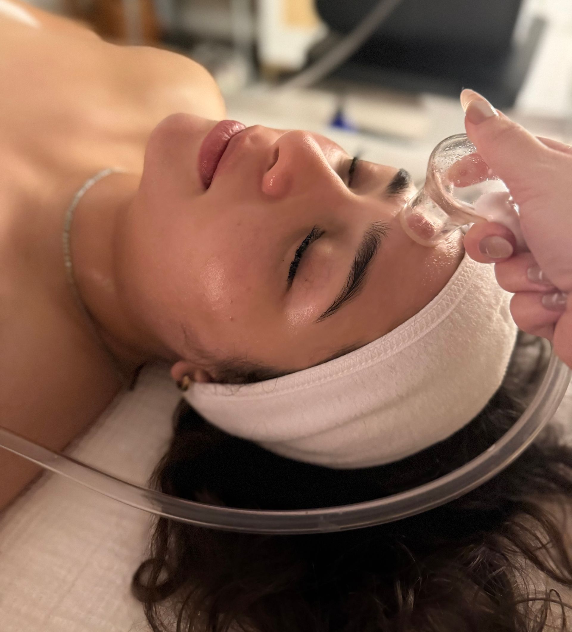 Woman receiving a facial massage with hands on her face, eyes closed.
