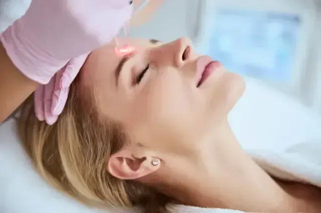Person receiving a facial treatment with a gloved hand applying product to the forehead