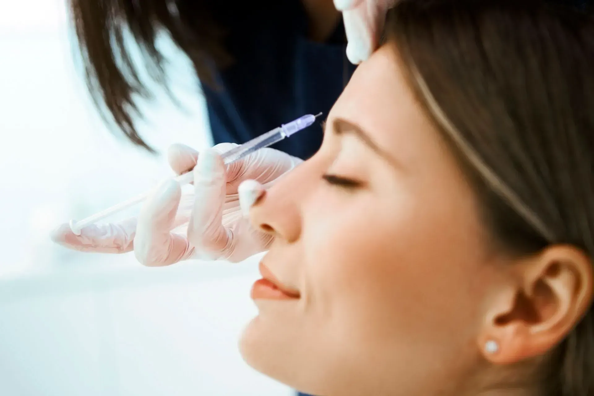 Cosmetologist injecting filler into a woman’s nose at a clinic