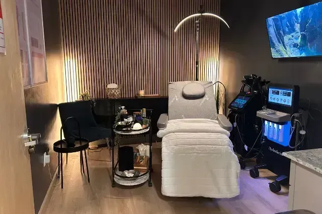 Quiet spa room with reclining treatment chair, black chair, small table, and monitor screens on the right