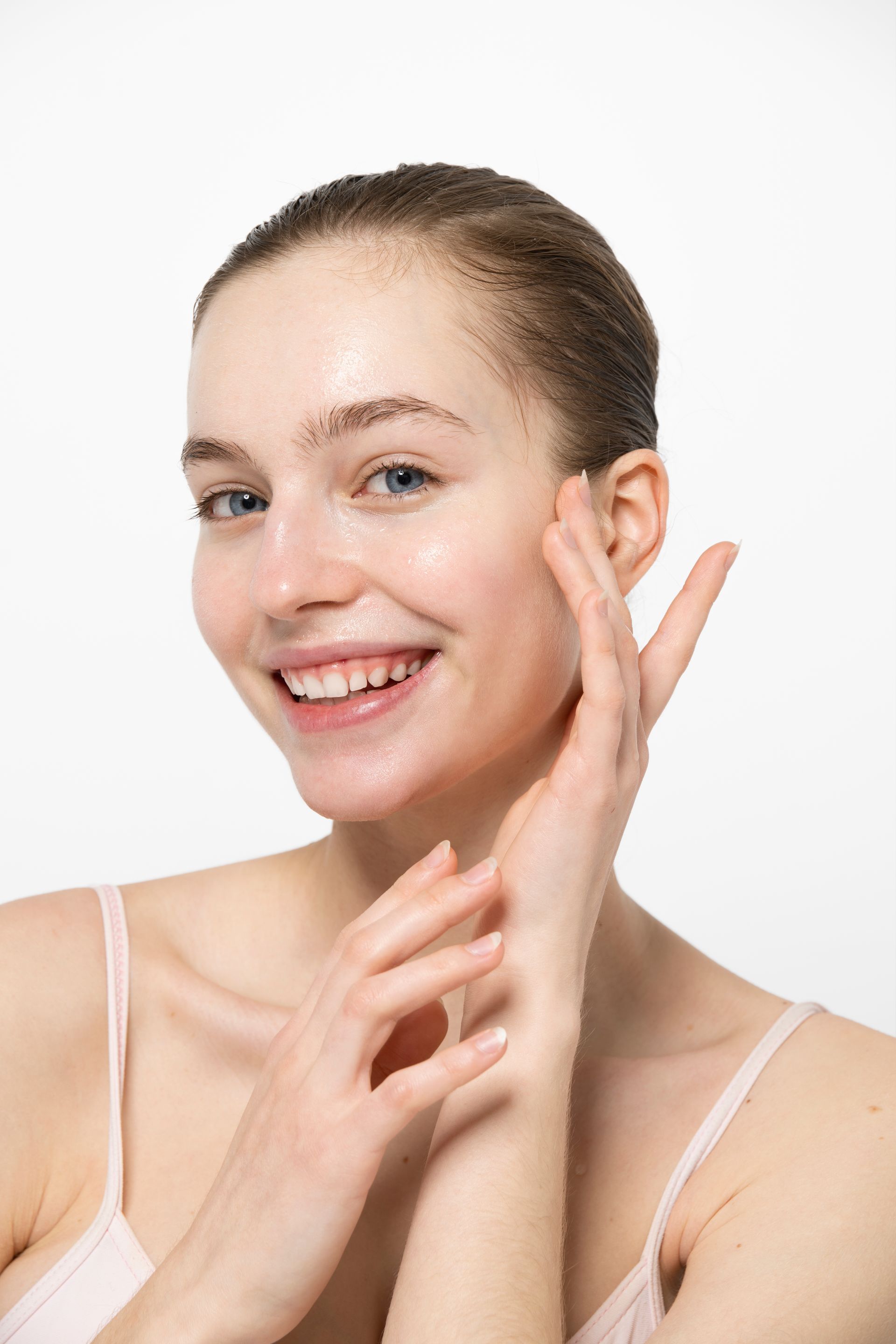 Smiling woman applying skincare cream to her cheek against a white background
