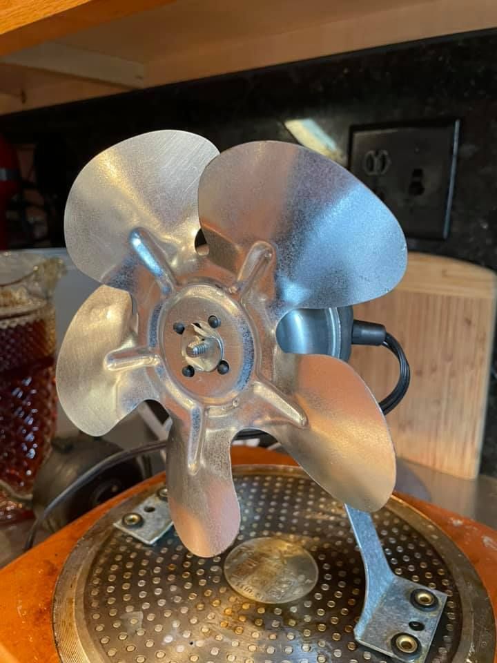 Silver metal fan with five blades, on a round base, near a power outlet.