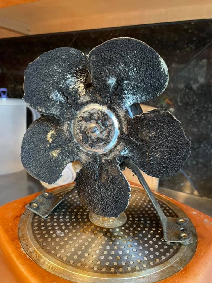 A small, vintage fan covered in black residue and a base of orange and silver.