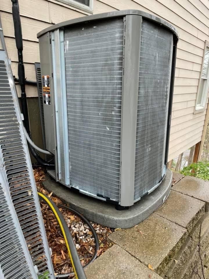 Air conditioning unit outdoors, gray metal, against a beige house.