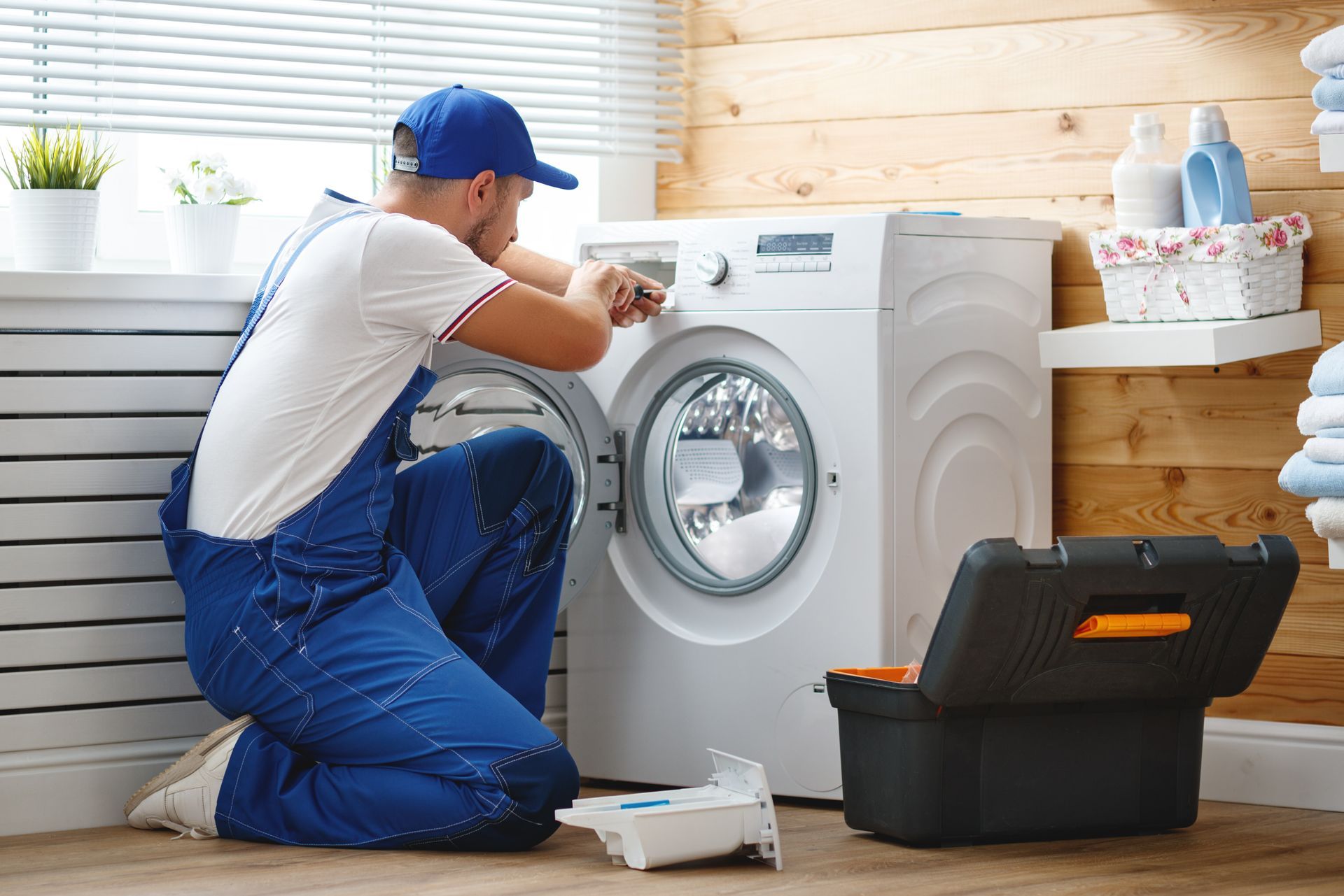 A technician performs residential appliance repair on a washing machine in the laundry.