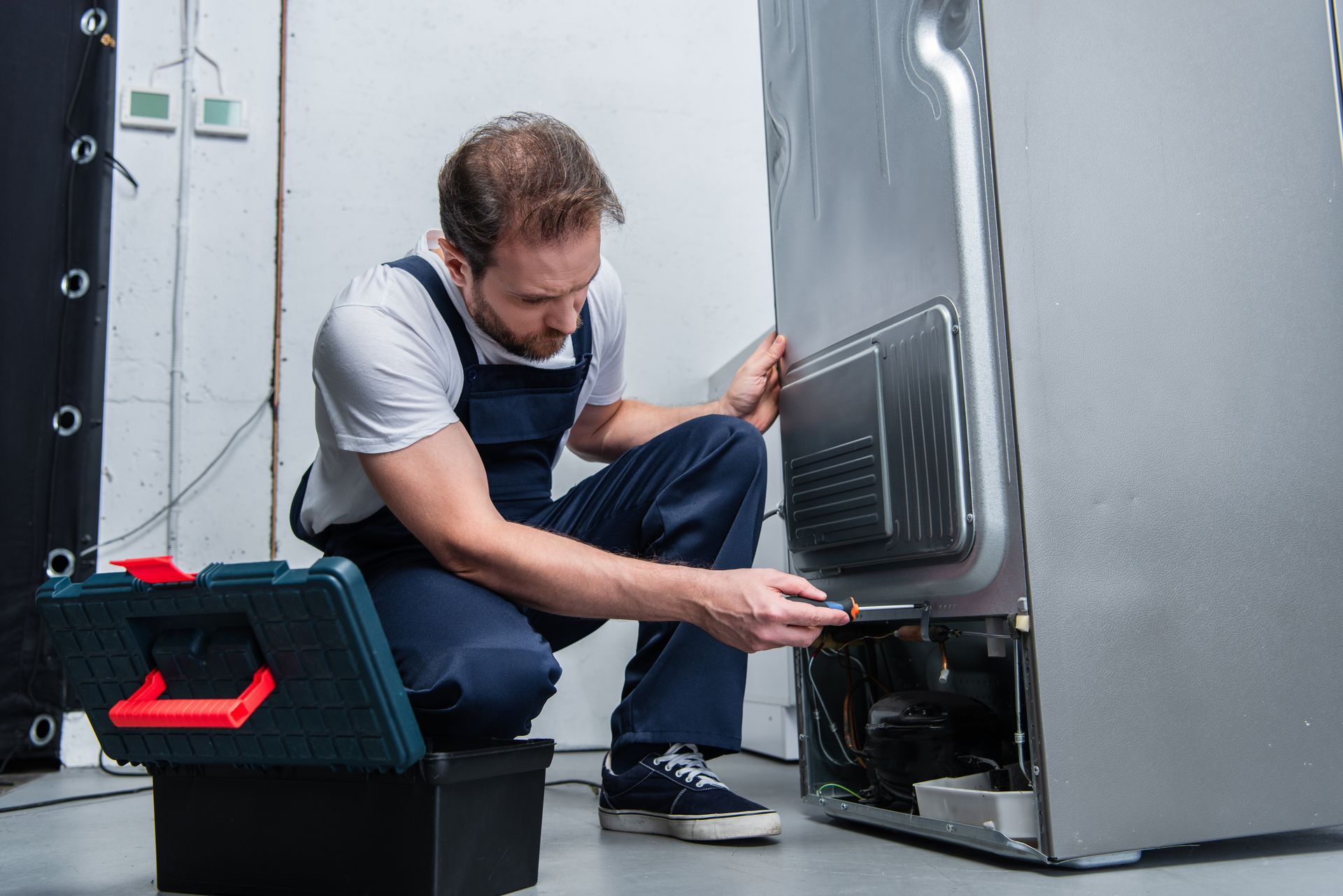 Appliance repair technician inspecting and fixing refrigerator compressor, performing maintenance. Appliance repair technician inspecting and fixing refrigerator compressor, performing maintenance.