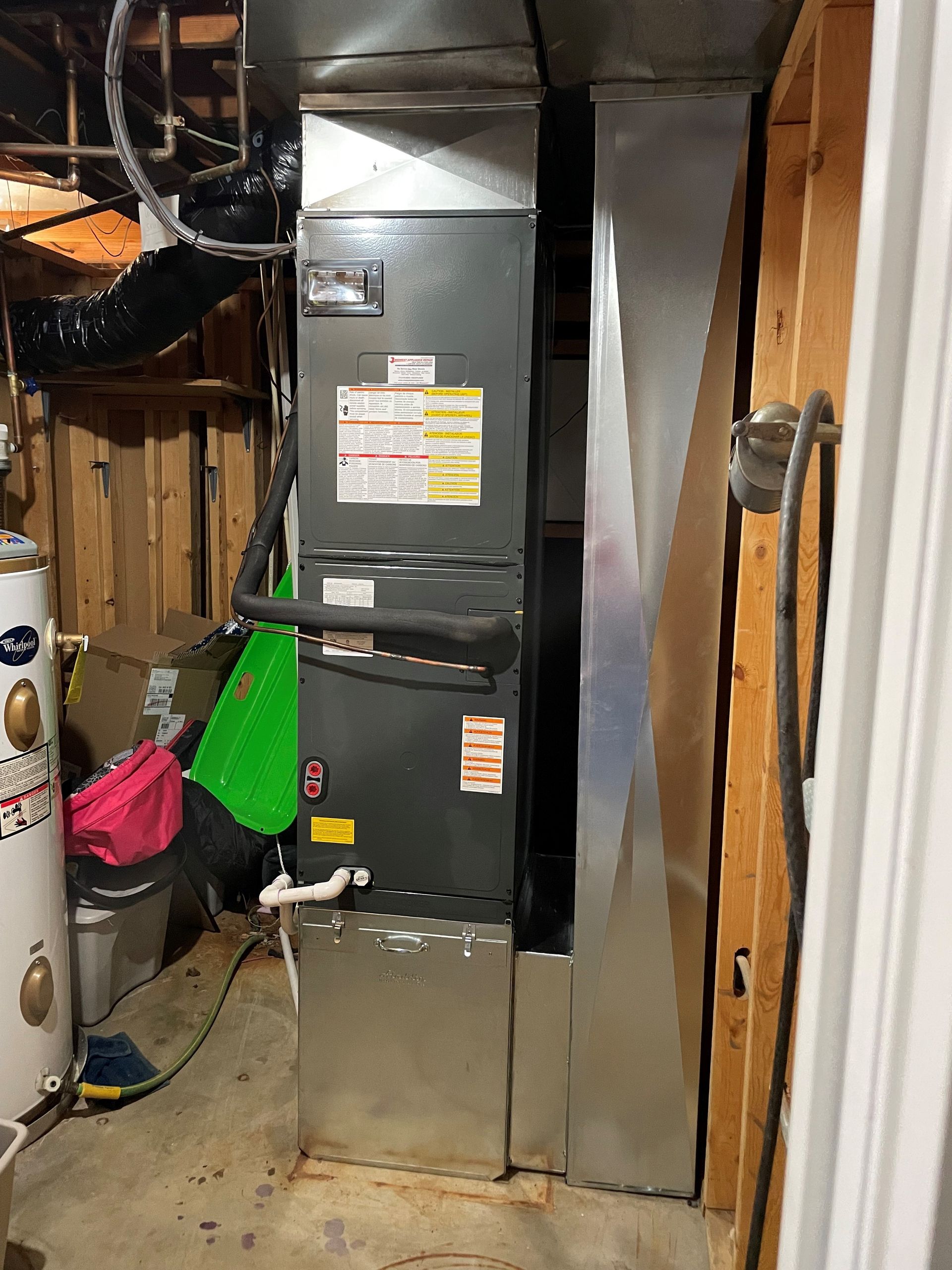 HVAC system installed in a basement. Rectangular metal unit with ductwork against a wooden wall.