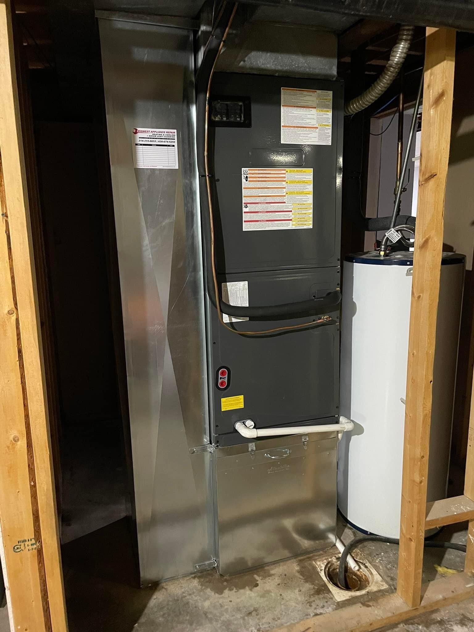 Furnace and water heater in a basement utility closet, with metal ductwork and wooden framing.