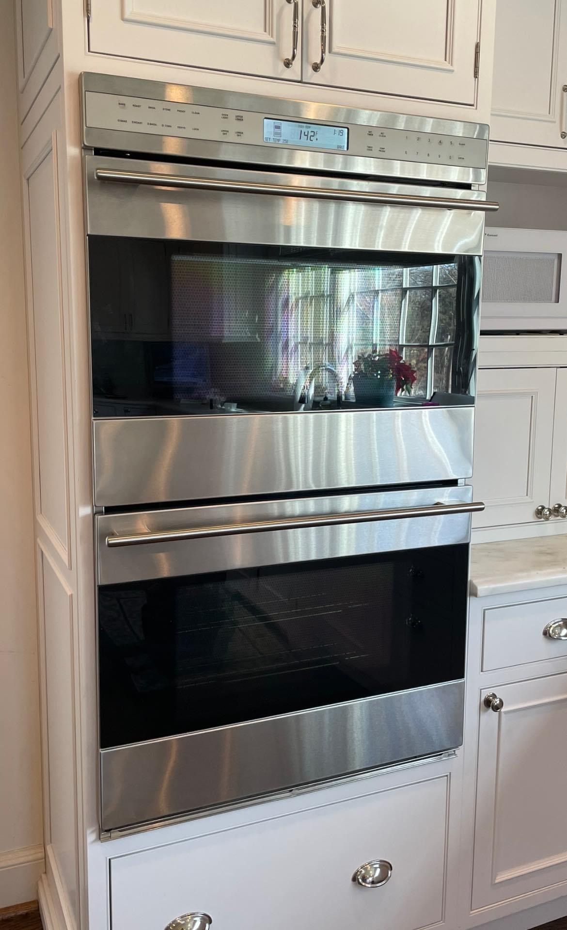 Stainless steel double oven built into white kitchen cabinets.