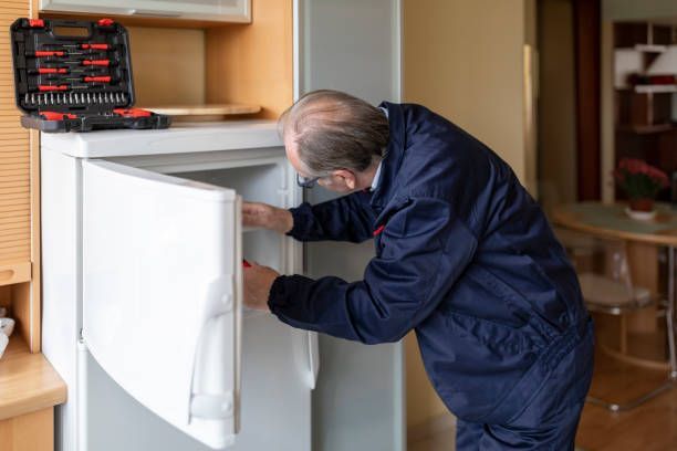 Technician performing fridge repair on a white refrigerator using tools from a kit on the counter. 