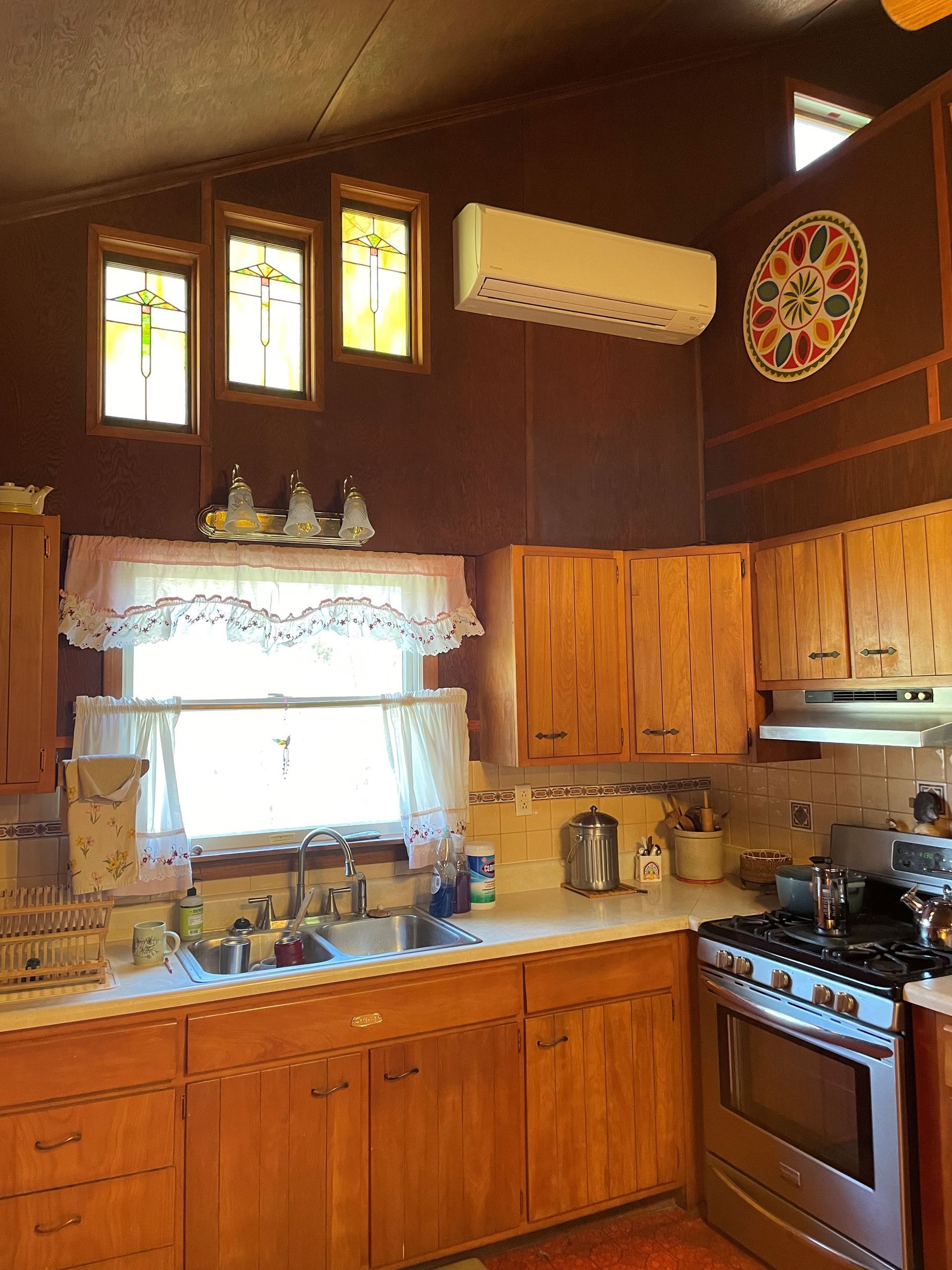 Kitchen with wood cabinets, stainless steel appliances, and an air conditioner. Small colorful windows.