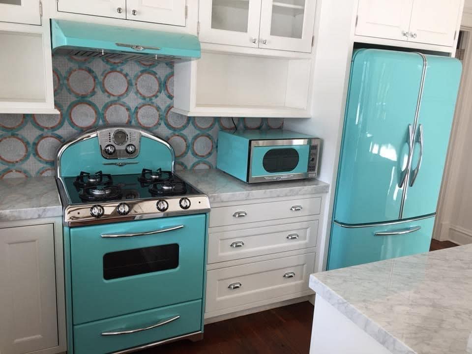 Turquoise retro kitchen with stove, fridge, microwave, white cabinets, and patterned backsplash.