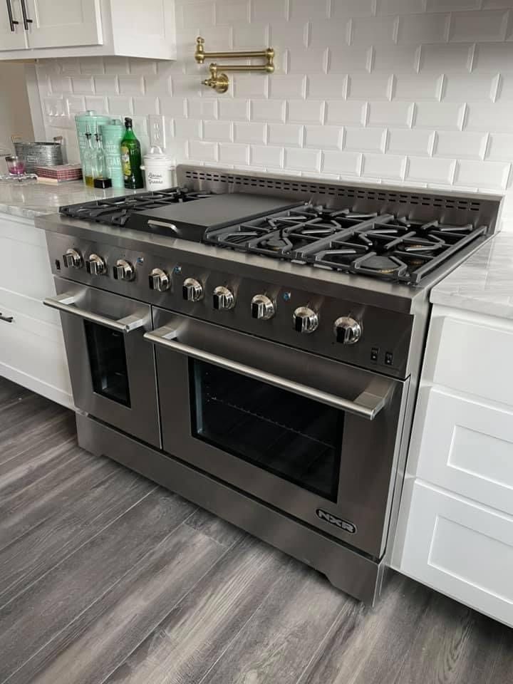 Stainless steel range with stovetop and two ovens in a kitchen.