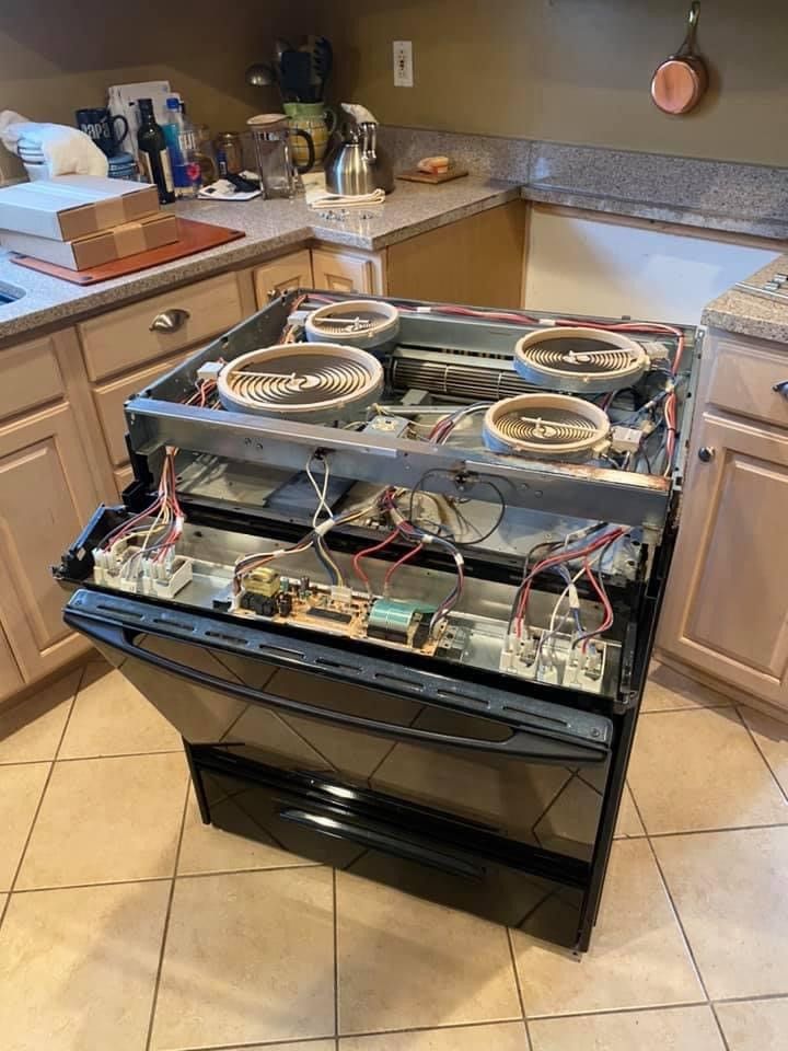 A black electric stove with the top pulled out, exposing wiring and heating elements, sits in a kitchen.