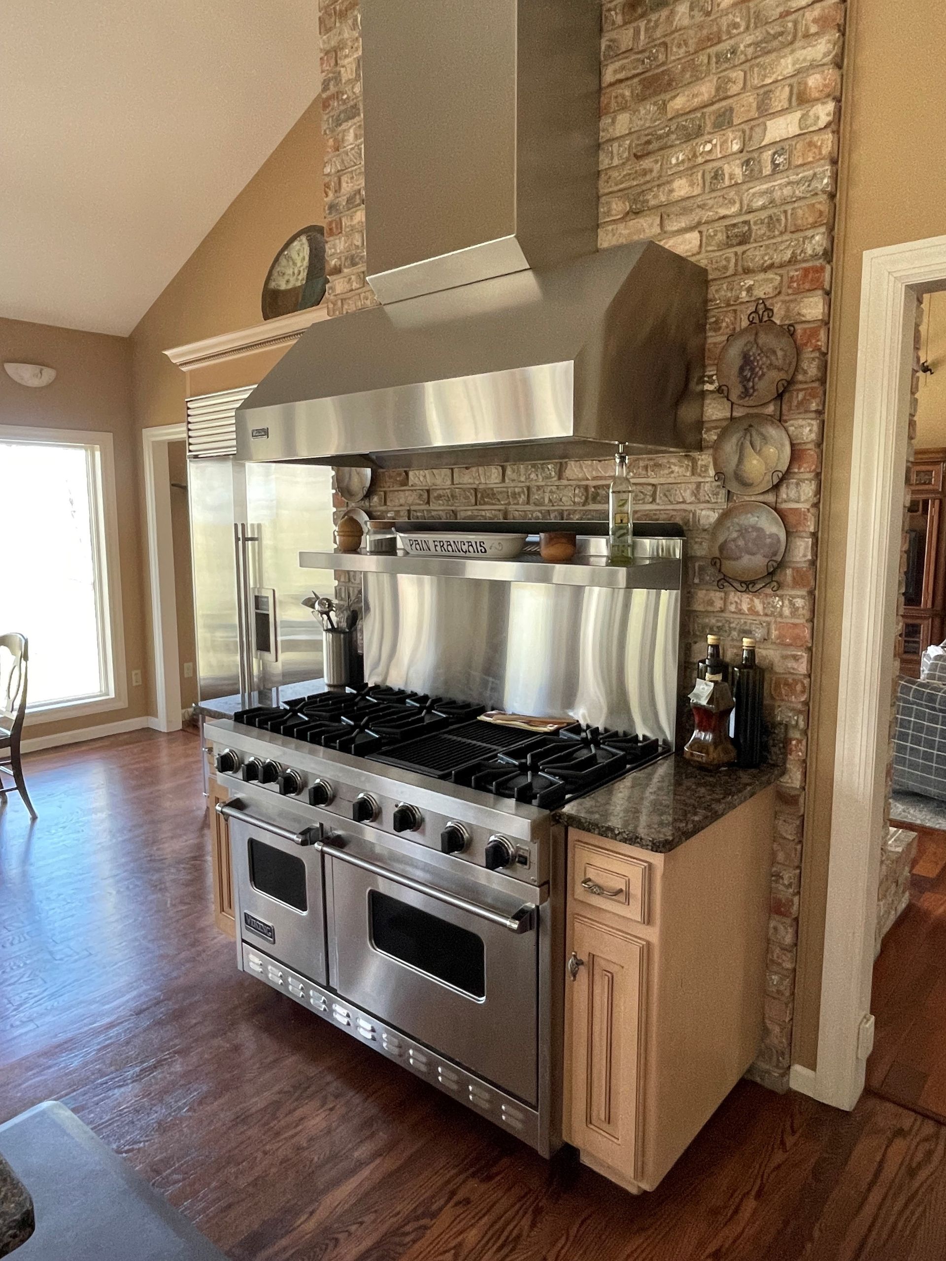 Stainless steel Viking range and vent hood against a brick wall in a kitchen with wood floors.