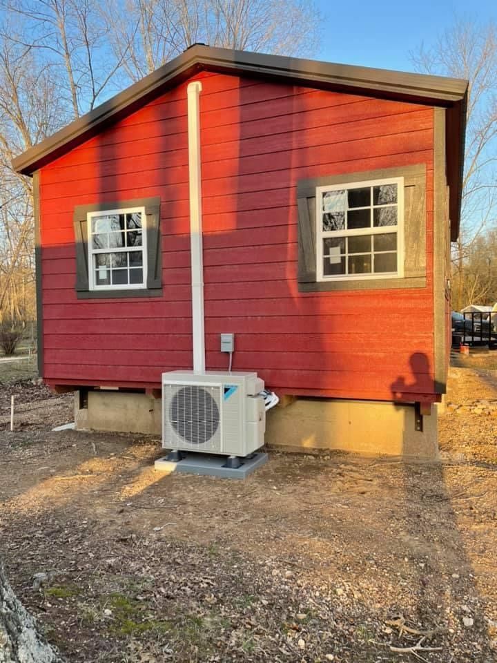 Red shed with air conditioning unit, white exhaust pipe, and two windows.