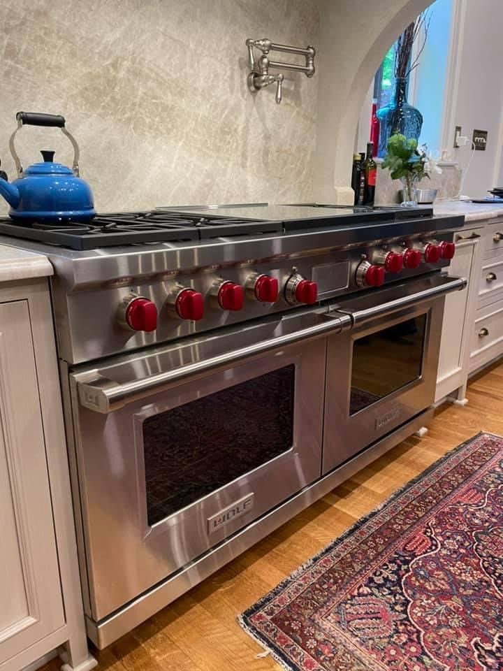 Stainless steel Wolf range with red knobs, blue kettle, and two ovens in a kitchen.